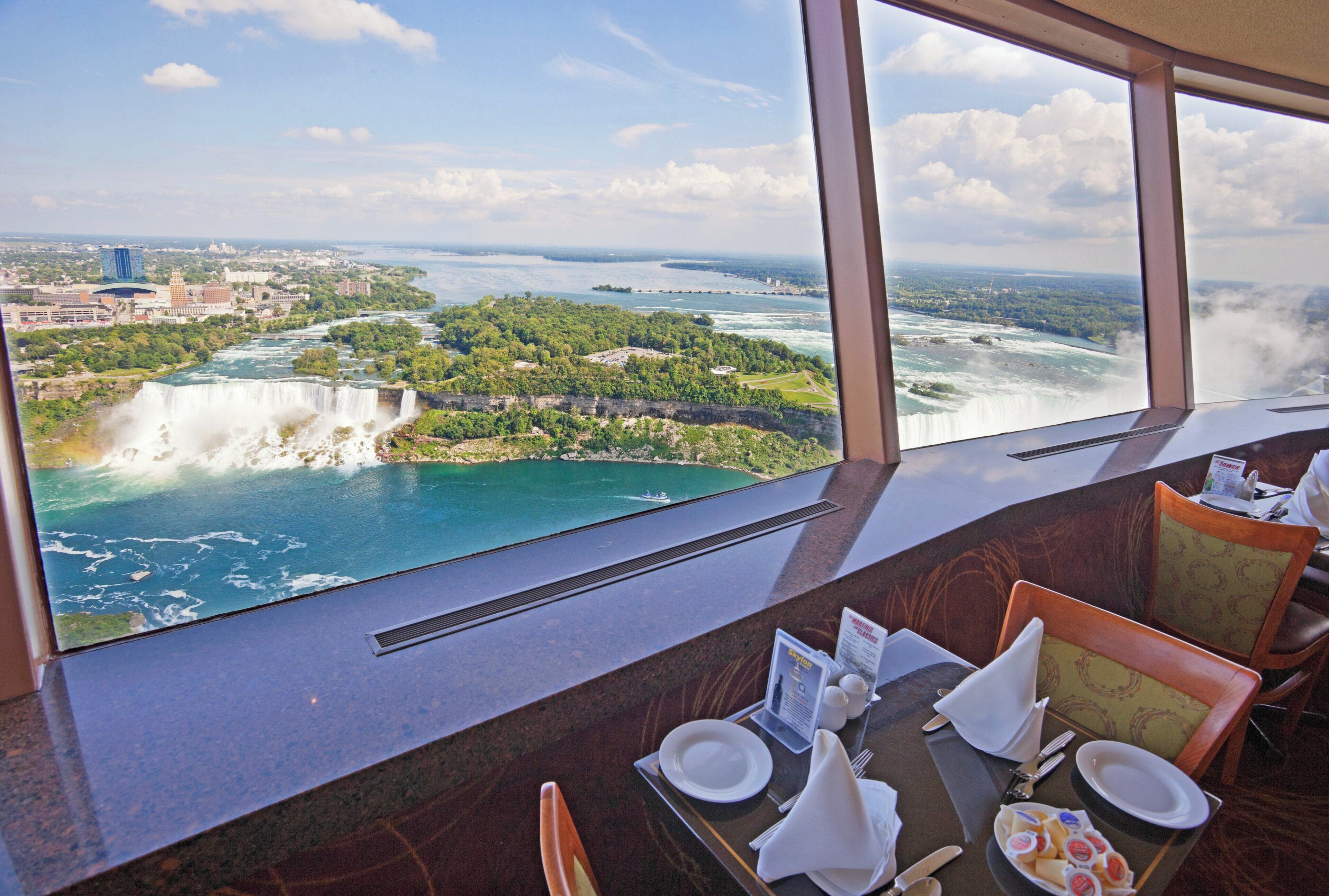 A dining area with a table set for two, overlooking a waterfall and a river.