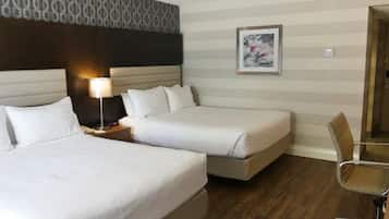 Una habitación de hotel con dos camas individuales, una mesita de noche con lámpara, un cuadro en la pared y una silla.