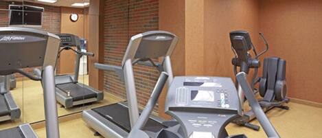Un gimnasio con cintas de correr, elípticas y un espejo grande.