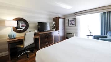 A hotel room with a large bed, a desk with a computer and TV, a chair, a wardrobe, and a window with curtains.