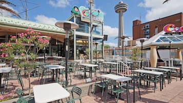 An outdoor patio area with tables and chairs, a building with a sign that reads 'Wood Terrace Grill House,' and a tower structure in the background.