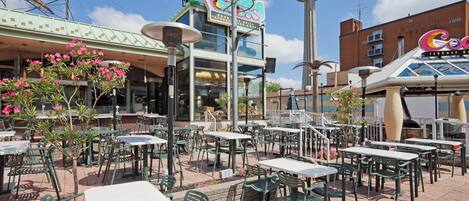 An outdoor patio area with tables and chairs, a building with a sign that reads 'Wood Terrace Grill House,' and a tower structure in the background.