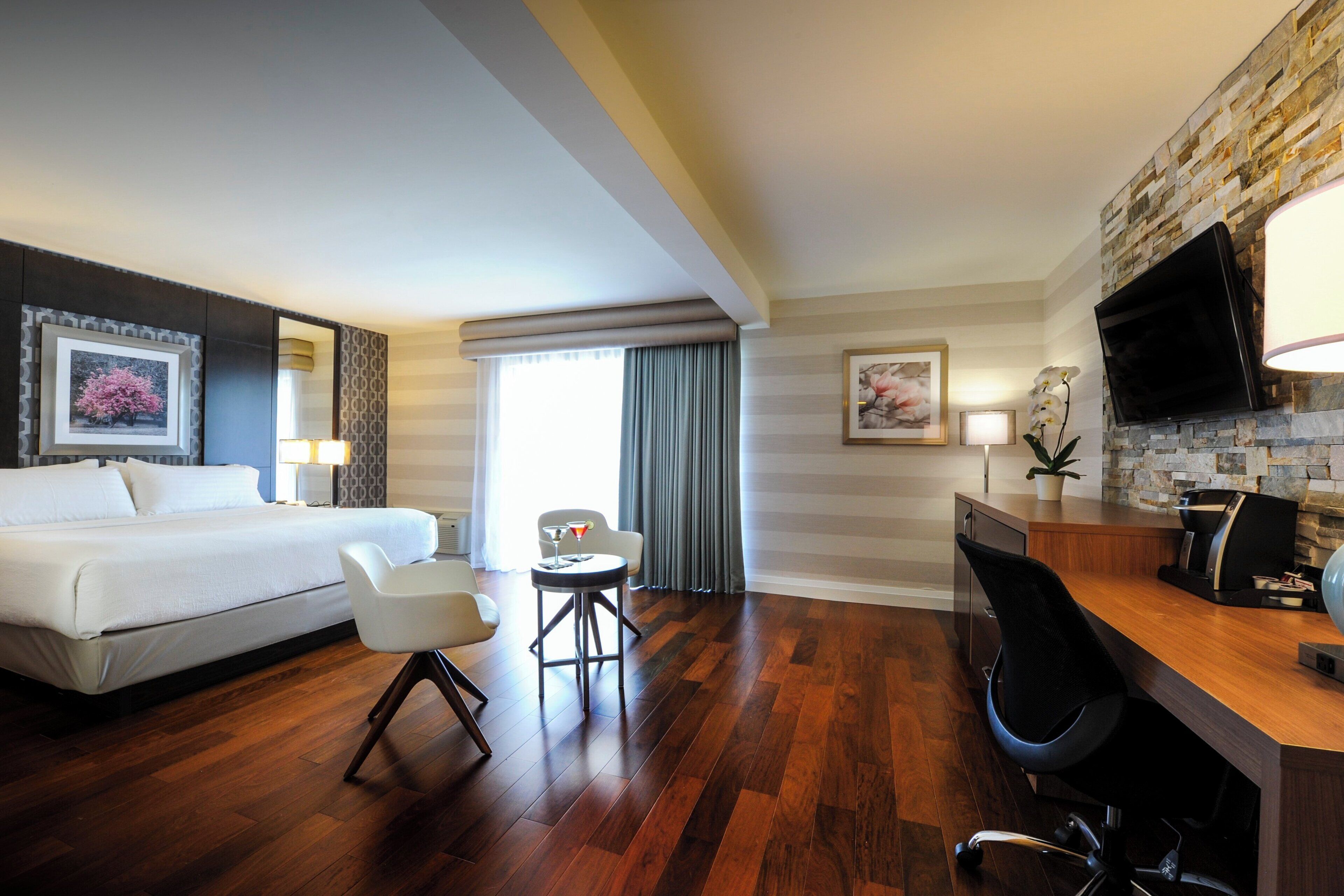 A hotel room with a bed, a desk, a chair, a coffee machine, and a TV.