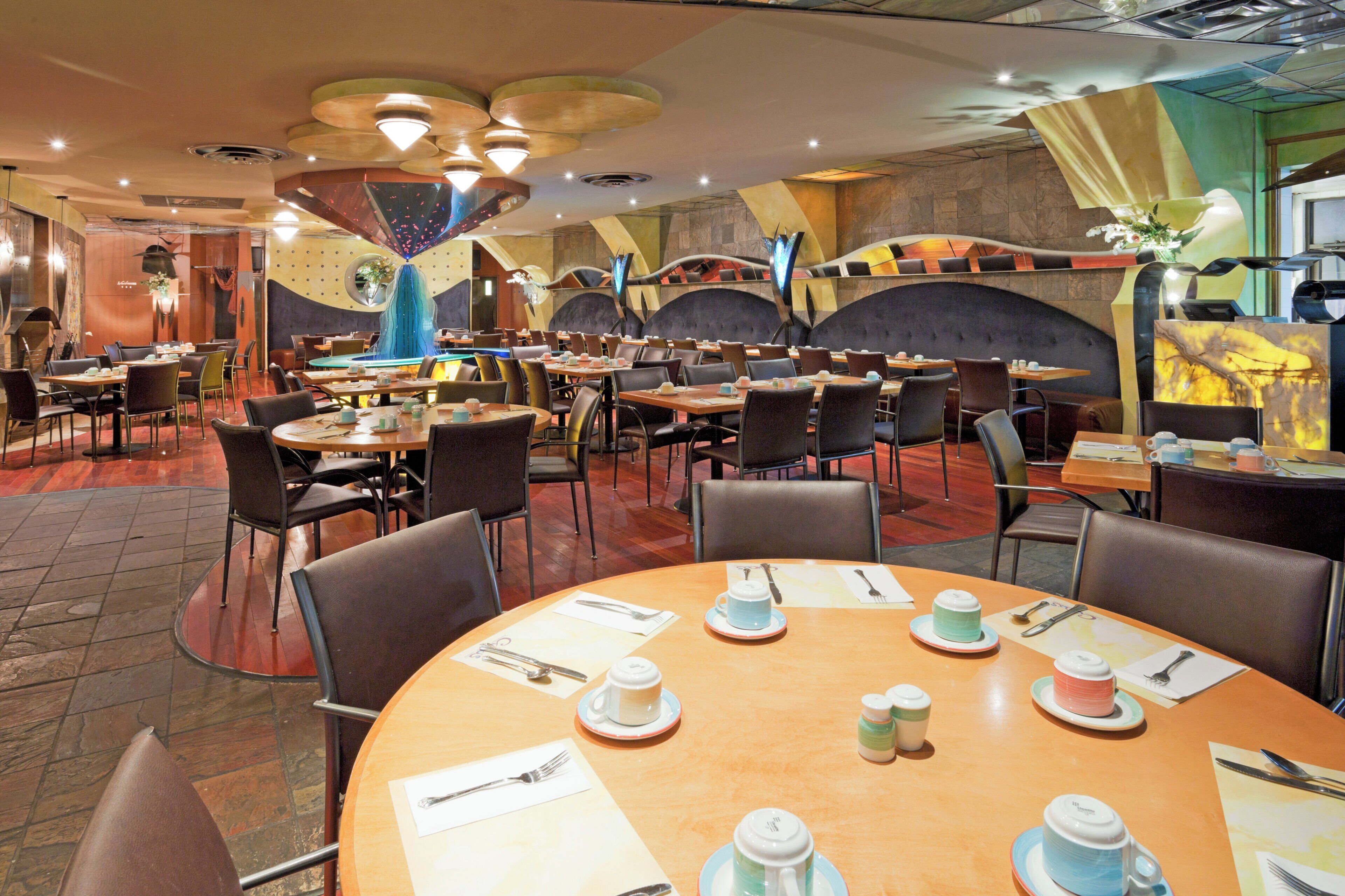 A restaurant with multiple dining tables, chairs, and a variety of table settings including cups, saucers, and cutlery.