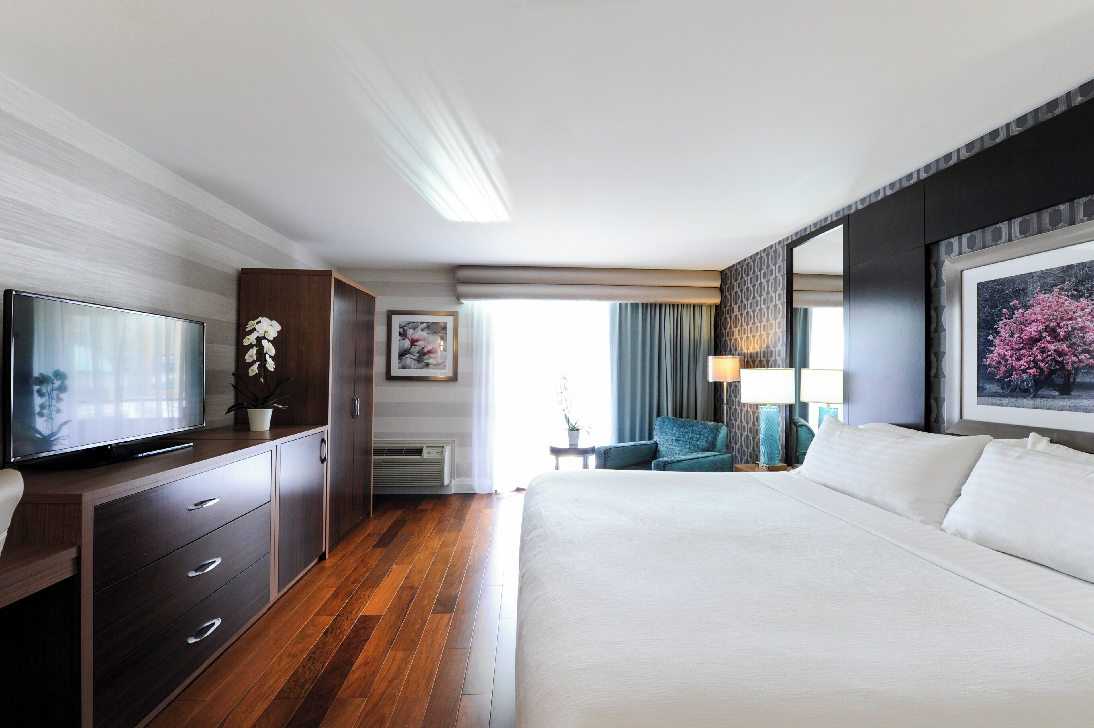 A hotel room with a bed, a TV, a desk with drawers, a chair, and a window with curtains.