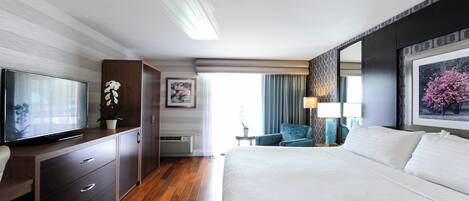 A hotel room with a bed, a TV, a desk with drawers, a chair, and a window with curtains.