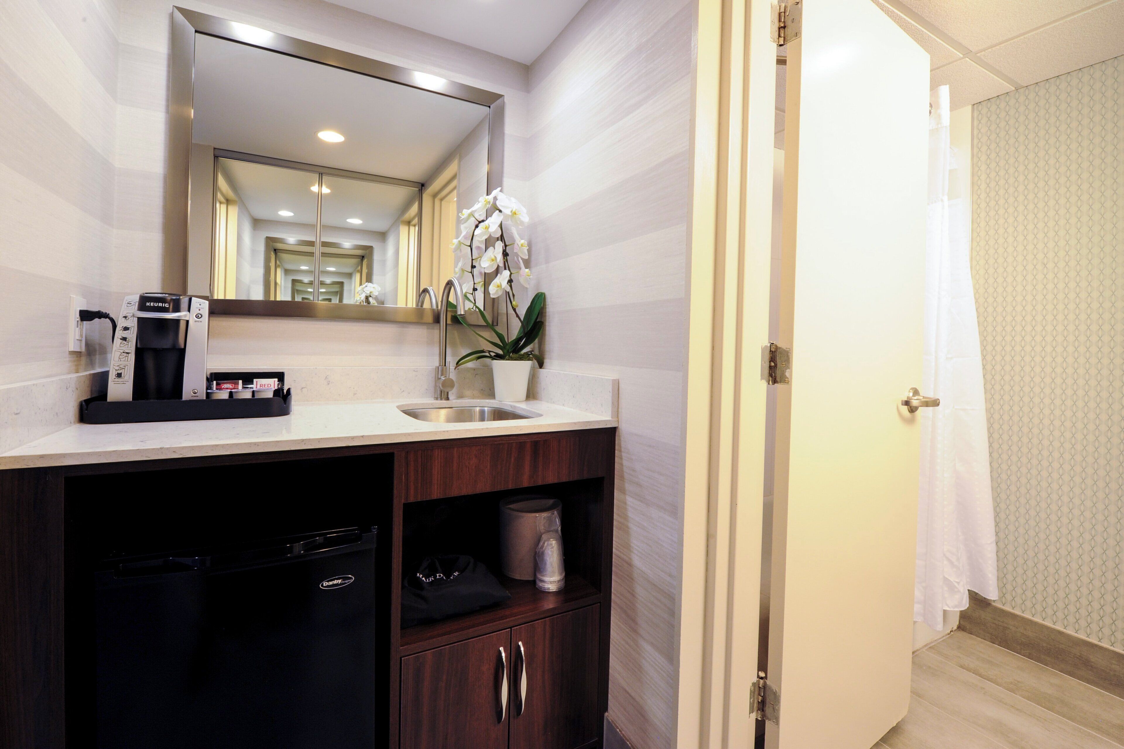 A hotel bathroom with a sink, mirror, and a coffee machine.