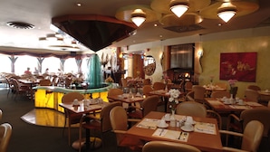 Ein Restaurant mit mehreren Tischen und Stühlen, einer Theke in der Mitte und Blick ins Freie.