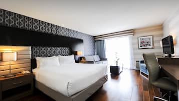 A hotel room with a large bed, a desk with a chair, a TV, and a window with curtains.