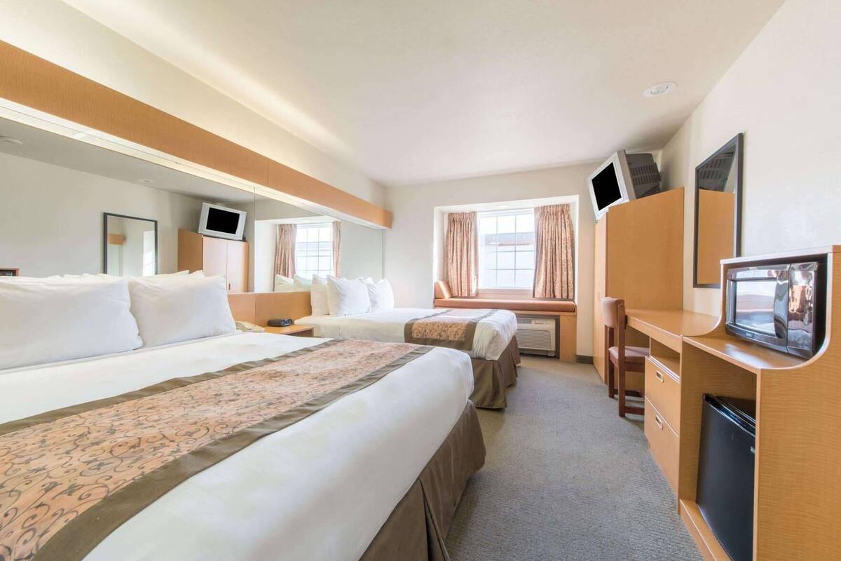 A hotel room with two beds, a desk with a television, a mirror, and a window with curtains.