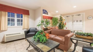 A reception area with a brown leather sofa, a black leather chair, a tiled coffee table with a plant centerpiece, and a potted plant on a side table. - Microtel Inn & Suites by Wyndham Altus (Altus)