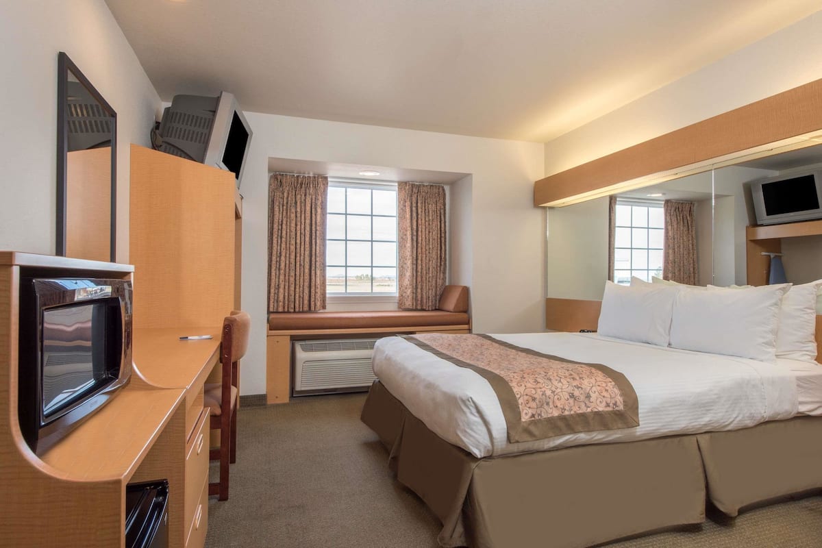 A hotel room with a bed, a desk with a TV, a window with curtains, and a mirror.