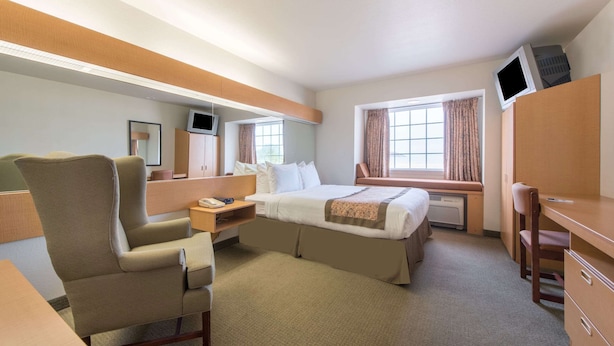A hotel room with a bed, a desk, a chair, a TV, and a window with curtains. - Microtel Inn & Suites by Wyndham Altus (Altus)