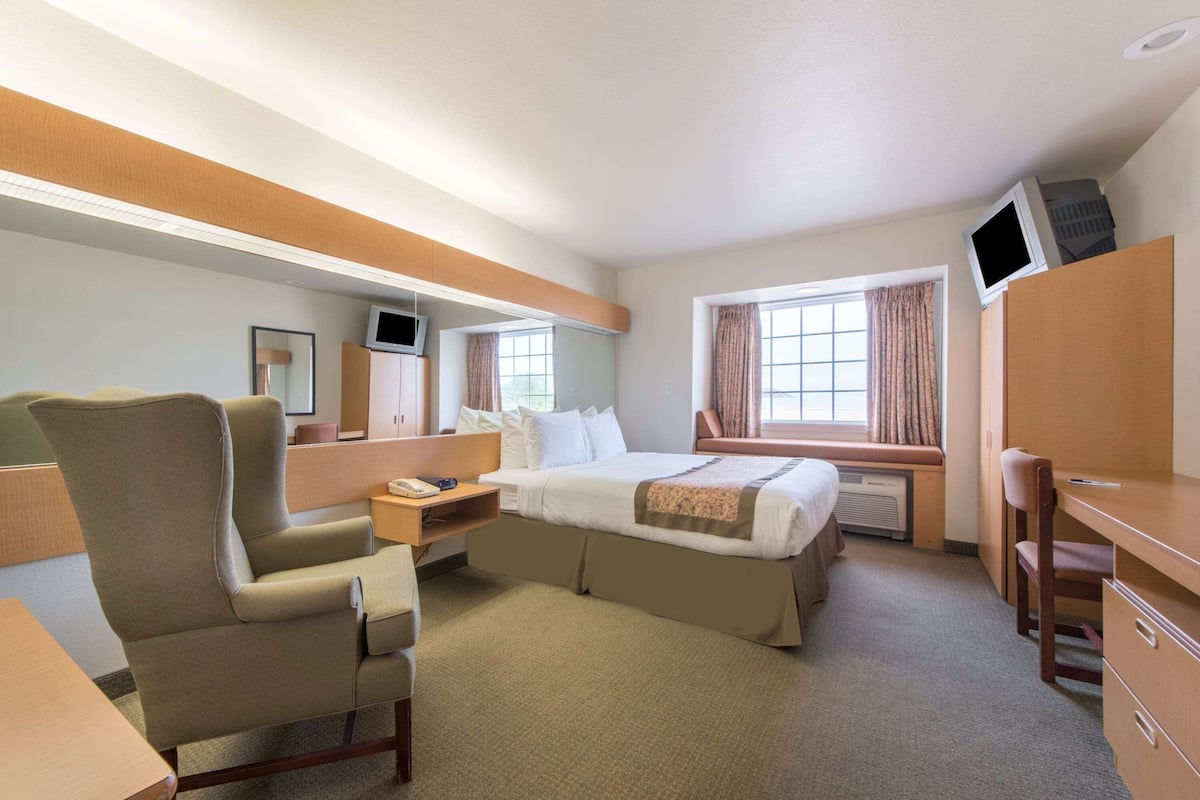 A hotel room with a bed, a desk, a chair, a TV, and a window with curtains.