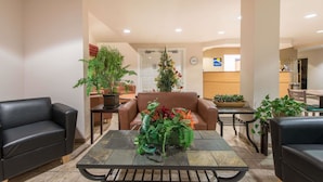 A lobby with a brown leather sofa, a black leather armchair, a table with a potted plant, and a reception desk in the background. - Microtel Inn & Suites by Wyndham Altus (Altus)