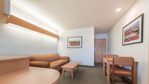 A modern room with a wooden reception desk, a round table, a sofa, and a chair. There is a framed picture on the wall and a door in the background. - Microtel Inn & Suites by Wyndham Altus (Altus)
