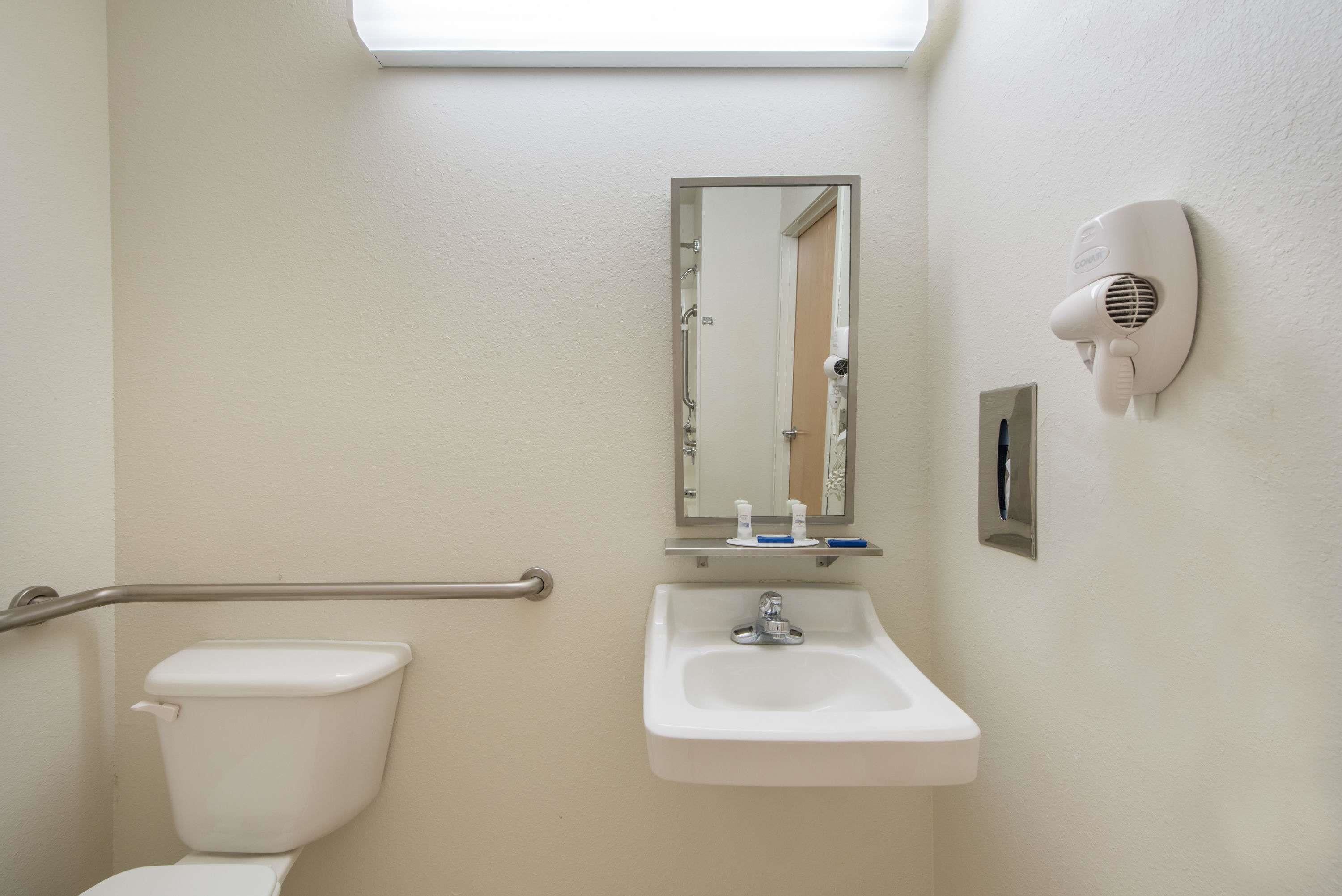Baño con inodoro, lavabo, espejo y secamanos.