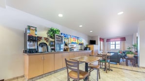 A kitchen area with a coffee machine, refrigerator, and microwave. There is a dining table with chairs and a sofa in the background. - Microtel Inn & Suites by Wyndham Altus (Altus)