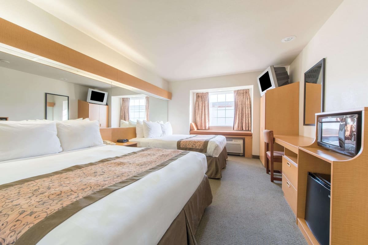 A hotel room with two beds, a desk with a computer, a TV, and a refrigerator.