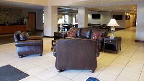 A spacious lobby with a leather sofa set, a wooden staircase, and a dining area in the background. - Wingate by Wyndham Coon Rapids (Coon Rapids)