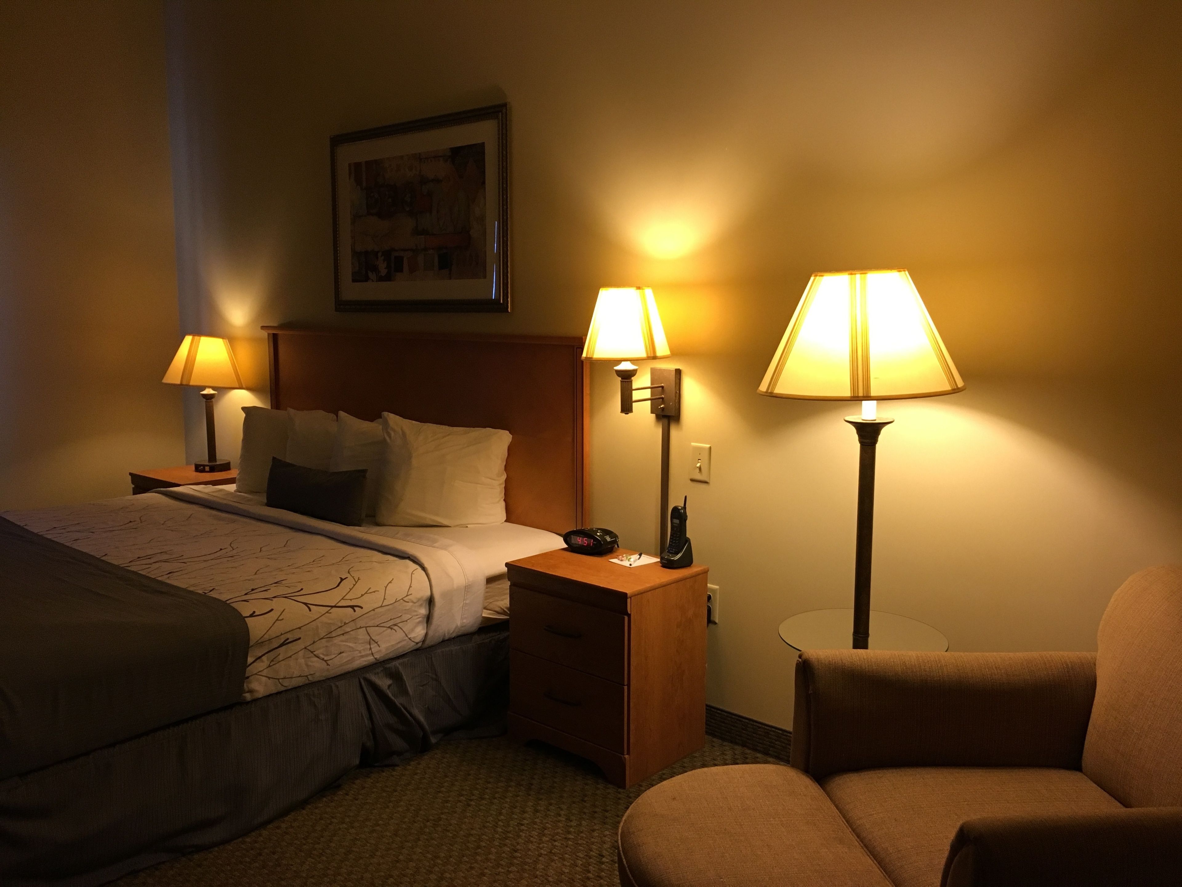Habitación de hotel con cama, dos lámparas de noche, mesita de noche, una silla y una pequeña mesa.