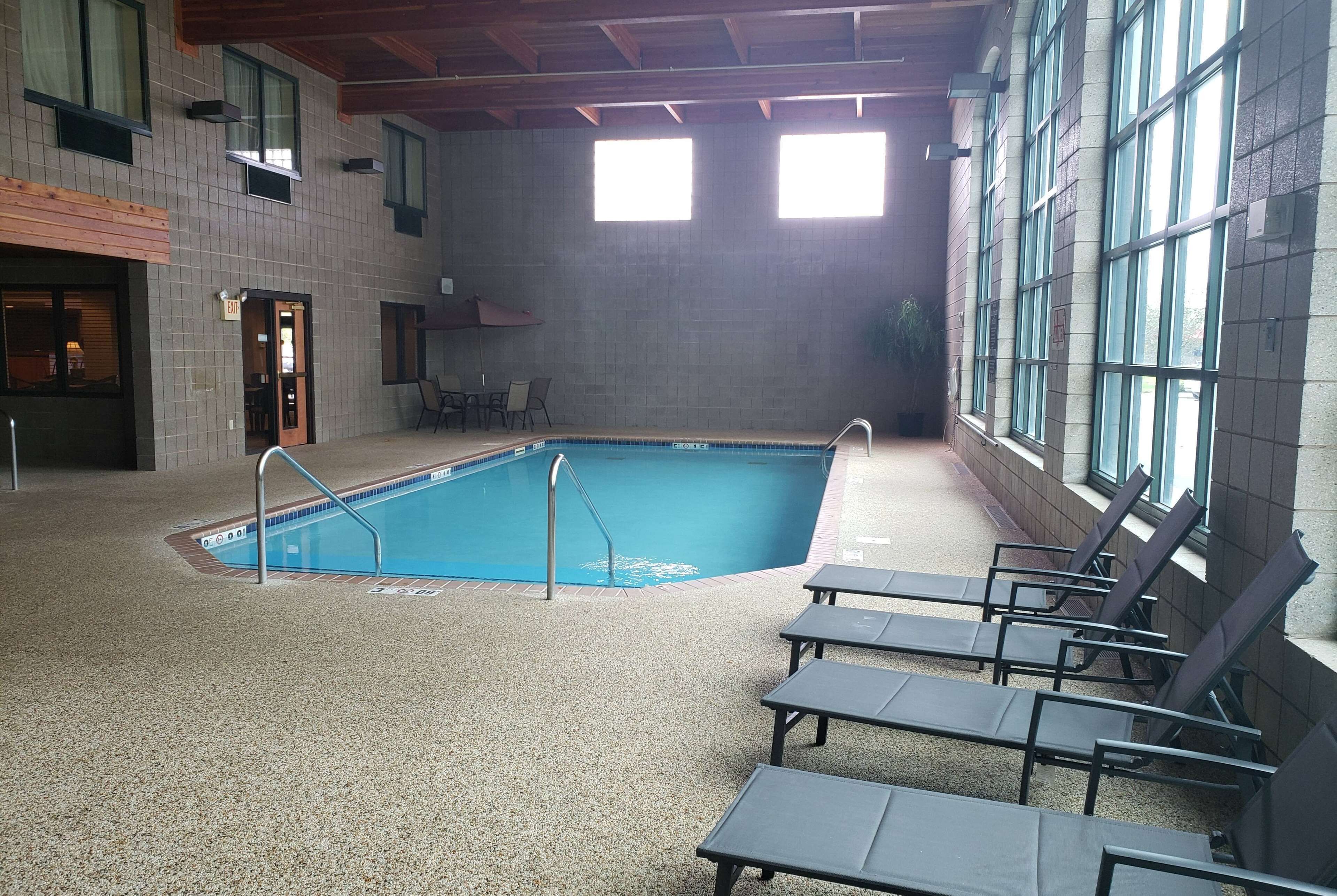 An indoor swimming pool with a tiled floor, a pool ladder, and lounge chairs.