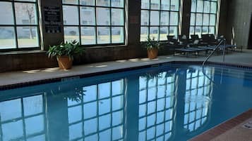 An indoor swimming pool with clear glass windows, potted plants, and a no diving sign.