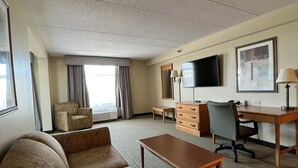 A hotel room with a sofa set, a desk, a chair, a television, and a window with curtains. - Wingate by Wyndham Coon Rapids (Coon Rapids)