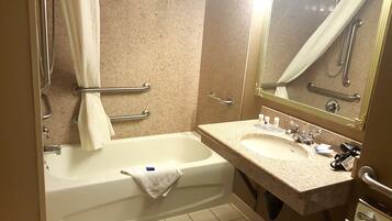 A bathroom with a bathtub, a sink, and a mirror. There are handrails and a towel rack.