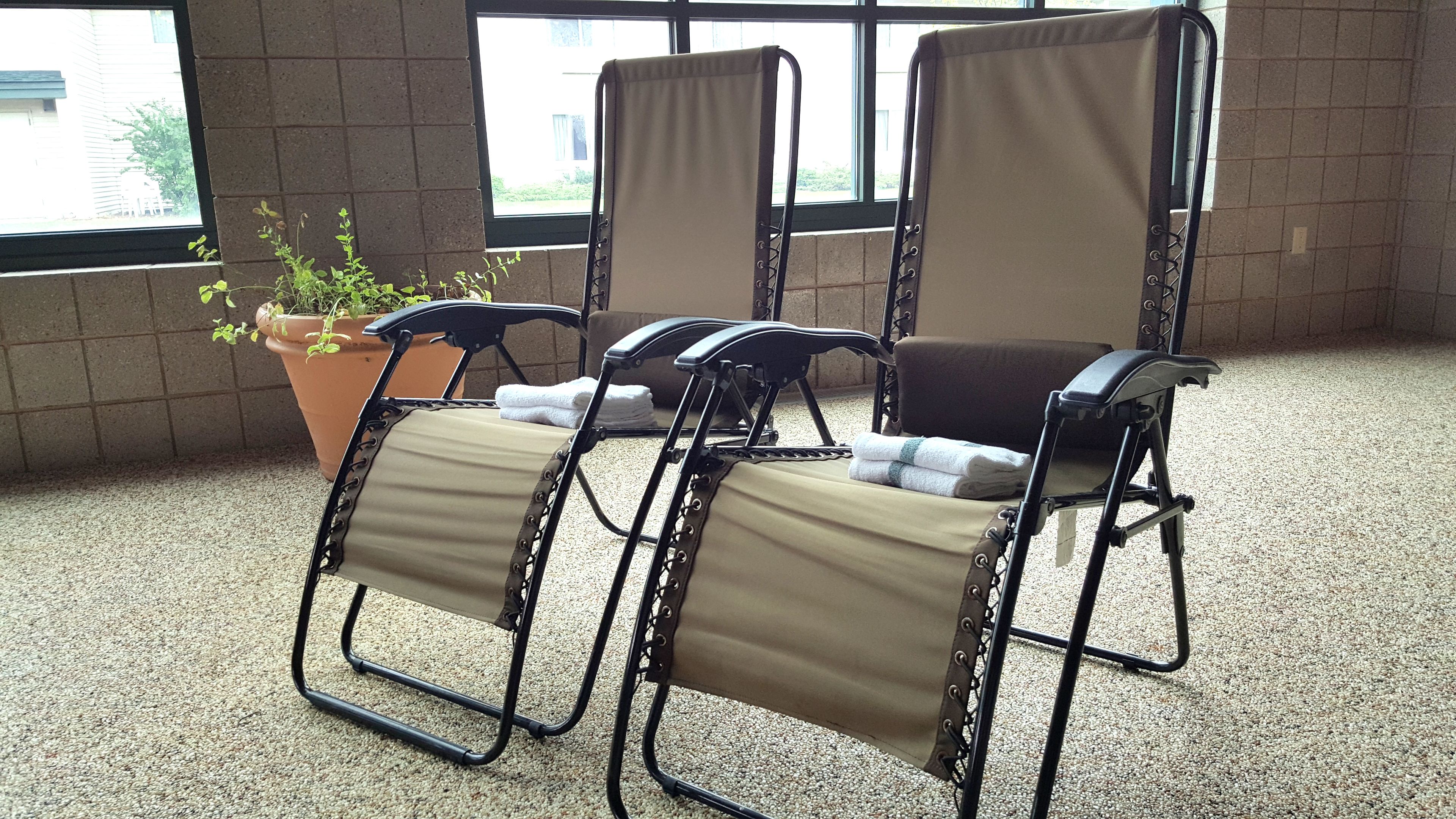 A room with three reclining chairs with beige cushions, a potted plant, and a window with a view of a building.