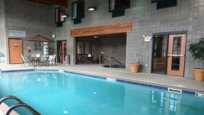 A pool area with a tiled floor, a wooden deck, and a seating area with chairs and tables. - Wingate by Wyndham Coon Rapids (Coon Rapids)