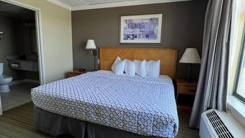 A hotel room with a large bed, a bedside table with a lamp, a wall-mounted artwork, and a window with curtains.