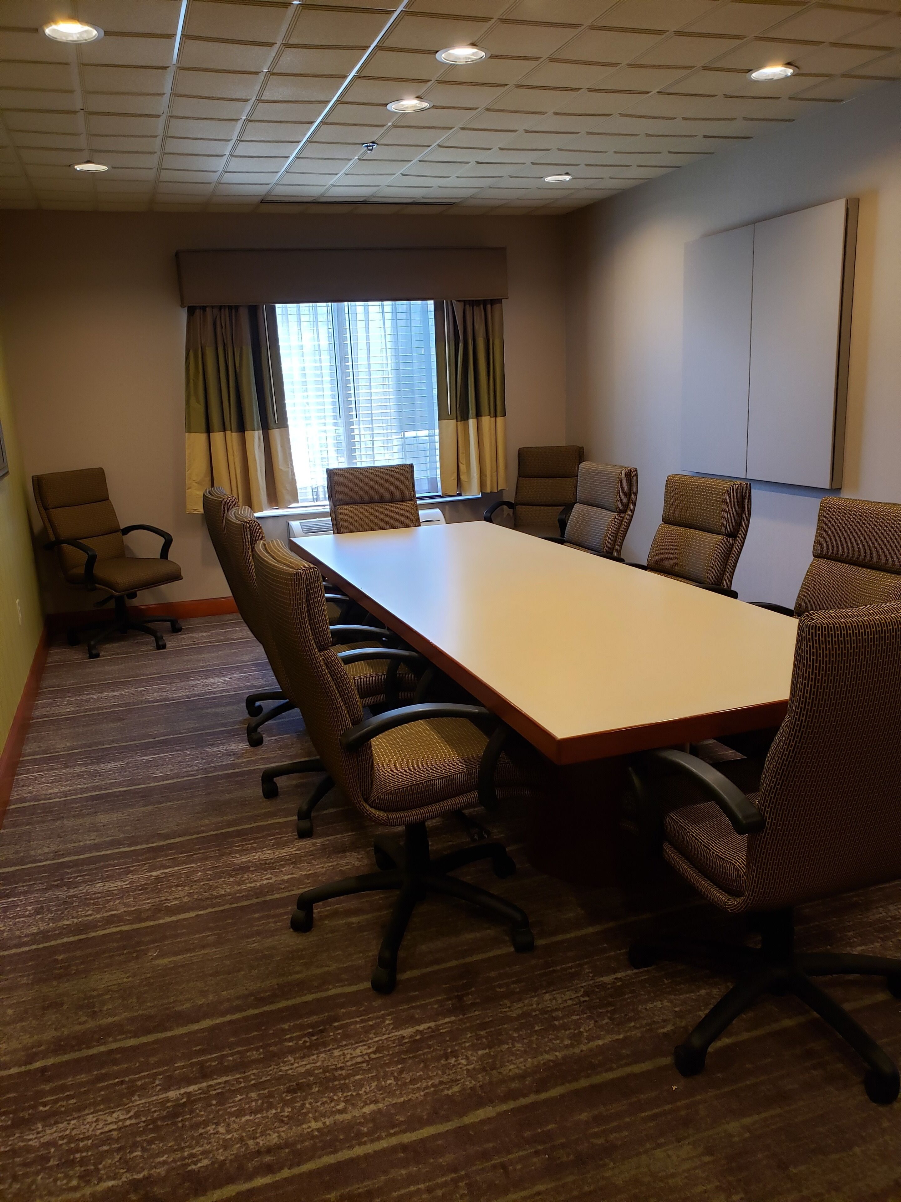 A conference room with a long table, six chairs, and a large window with curtains.