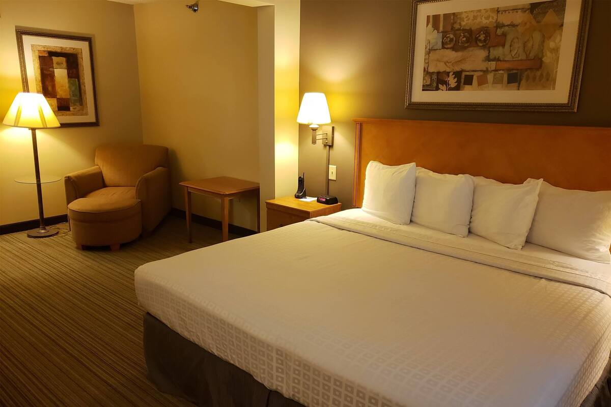 A hotel room with a large bed, a chair, a desk, and two lamps.