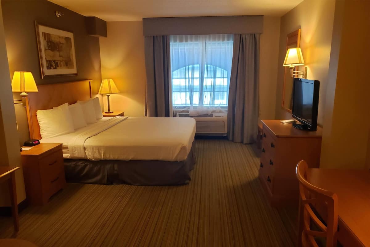 A hotel room with a bed, bedside lamps, a television, a desk, and a window with curtains.