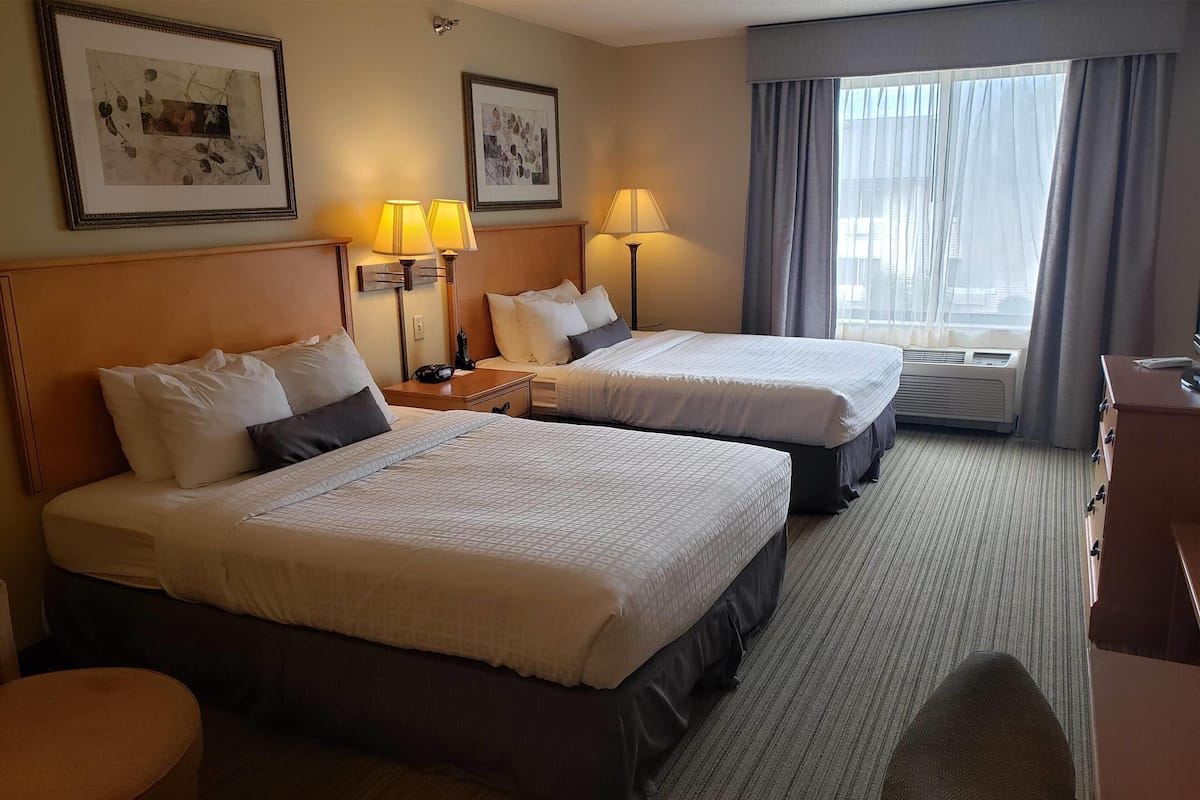 A hotel room with two beds, a desk, a chair, and a window with curtains.