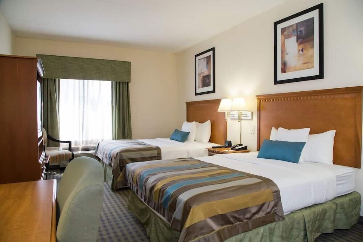Une chambre d’hôtel avec deux lits, un bureau, une chaise, une lampe et une fenêtre avec des rideaux.