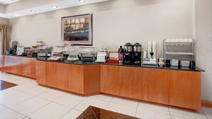Zona de recepción de hotel con una larga barra de mostrador, máquinas de café y una obra de arte enmarcada en la pared.