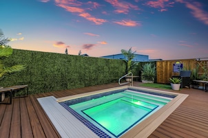Piscina com deck de madeira, rodeada por um conjunto de sebe verde e cerca de madeira.
