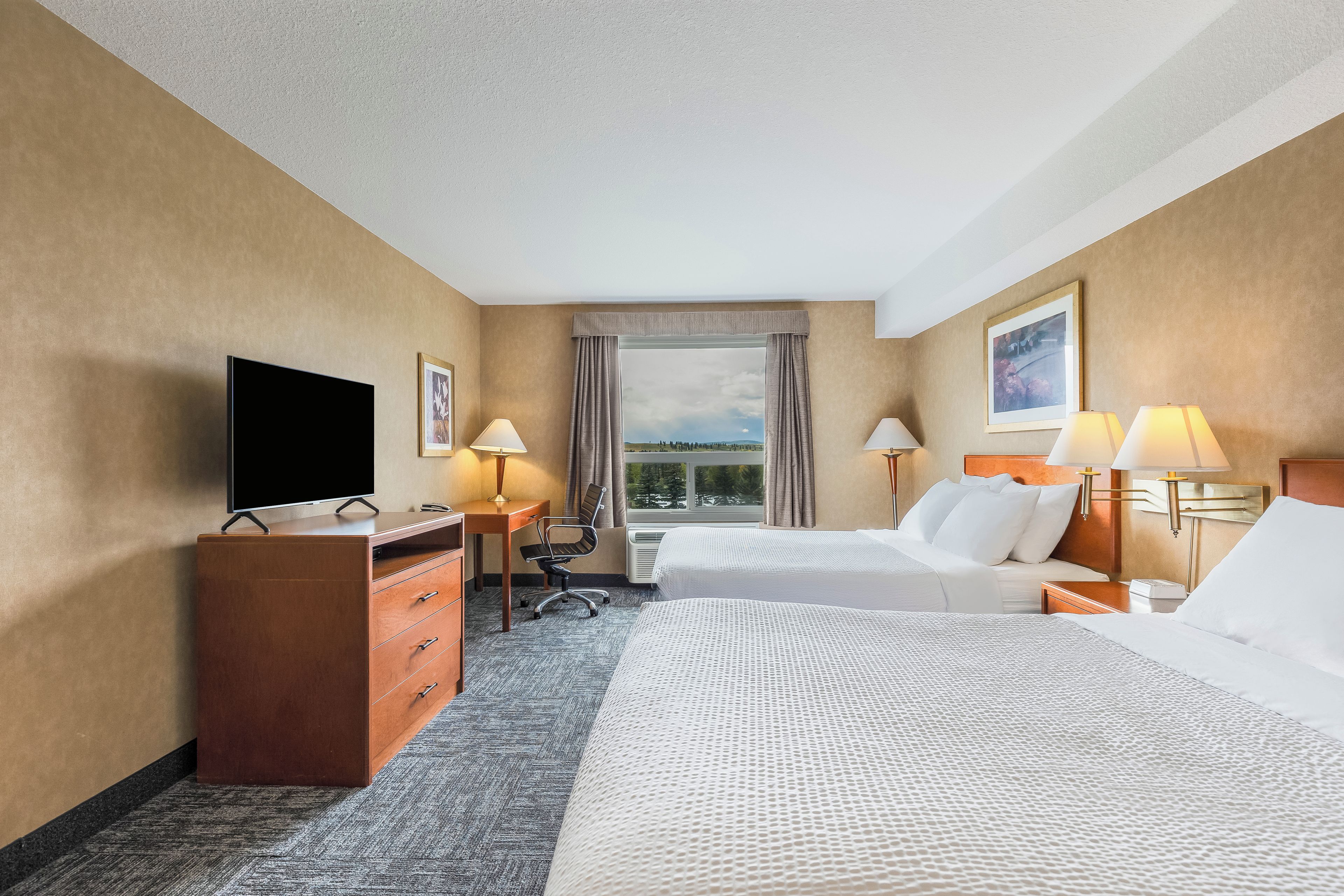 Een hotelkamer met een bed, bureau, stoel, televisie en twee lampen.
