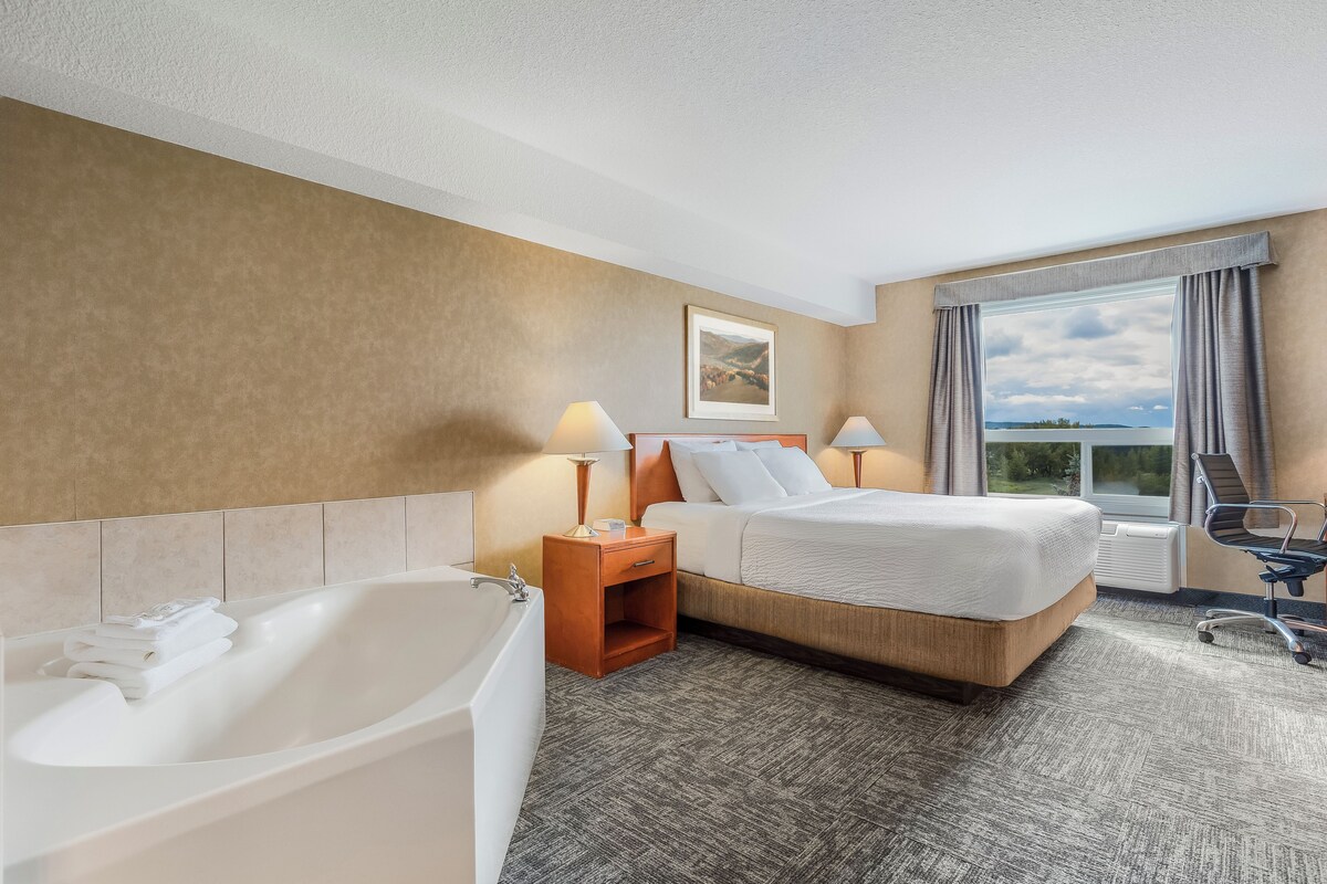 A hotel room with a large bed, a bathtub, a desk, and a window with a view.