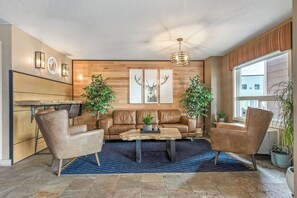 A modern living room with a brown leather sofa, two armchairs, a coffee table, and a wooden accent wall with framed deer antlers. - Days Inn & Suites by Wyndham Cochrane (Cochrane)