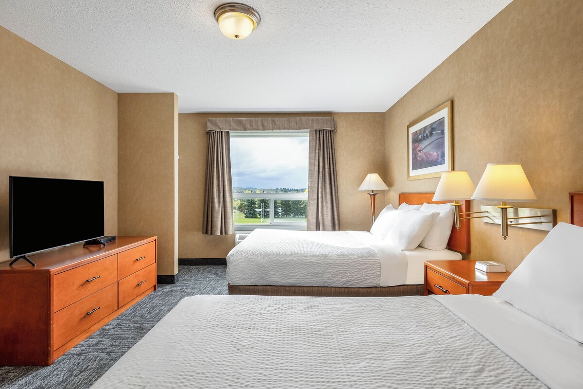A hotel room with a bed, a TV, a desk, and a window with curtains.