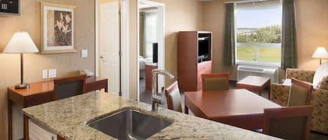 A hotel room with a granite countertop sink, a dining area with a table and chairs, a television, and a window with a view of the outdoors.