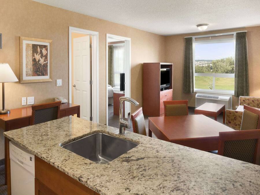 Une chambre d’hôtel dotée d’un lavabo avec un plan de travail en granit, d’un coin repas avec une table et des chaises, d’une télévision et d’une fenêtre donnant sur l’extérieur.