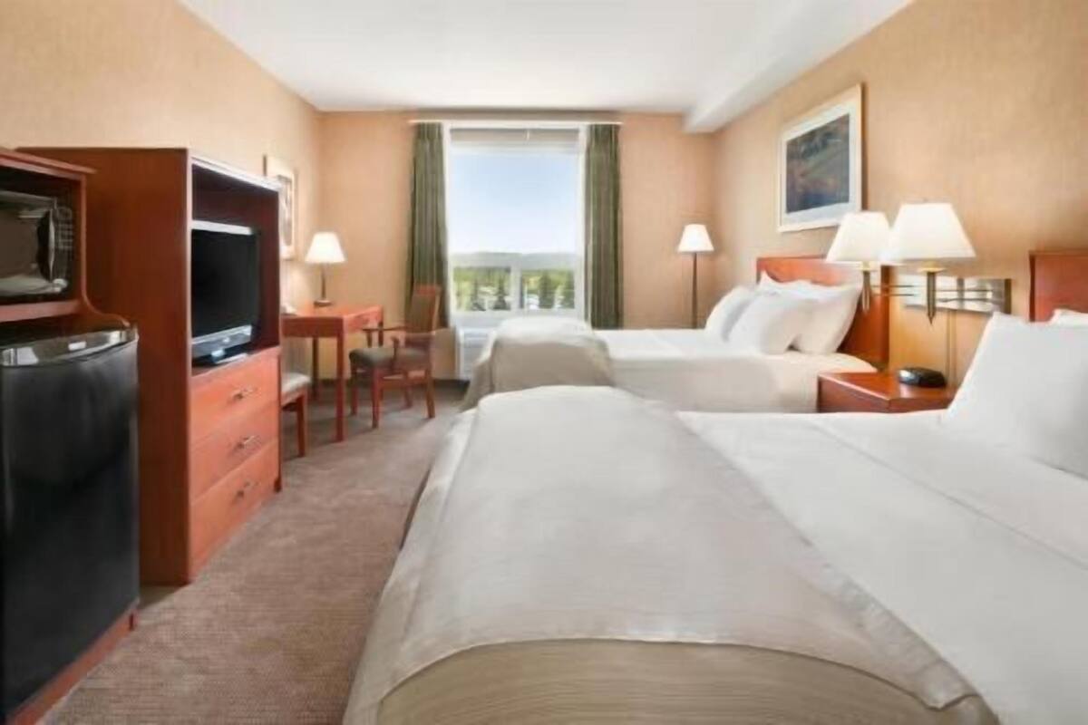 Una habitación de hotel con dos camas, televisión, escritorio y ventana.