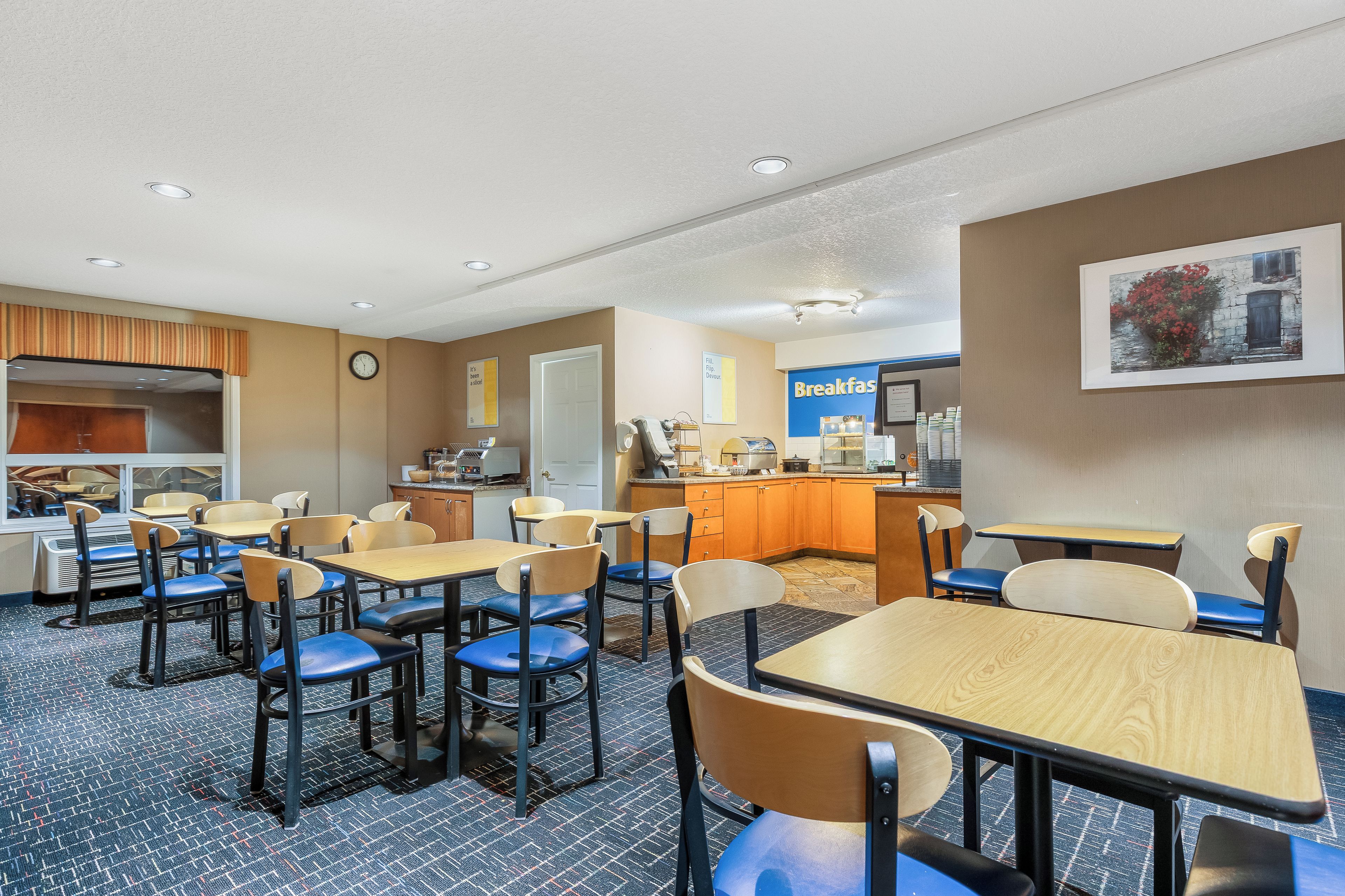 Een ontbijtruimte in een hotel met tafels, stoelen, een klok en een bord dat ontbijt aangeeft.