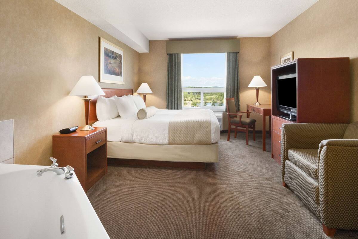 Habitación de hotel con cama, escritorio, televisor, silla, lámpara y bañera.