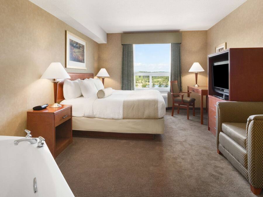 Ett hotellrum med en säng, ett skrivbord, en tv, en stol, en lampa och ett badkar.