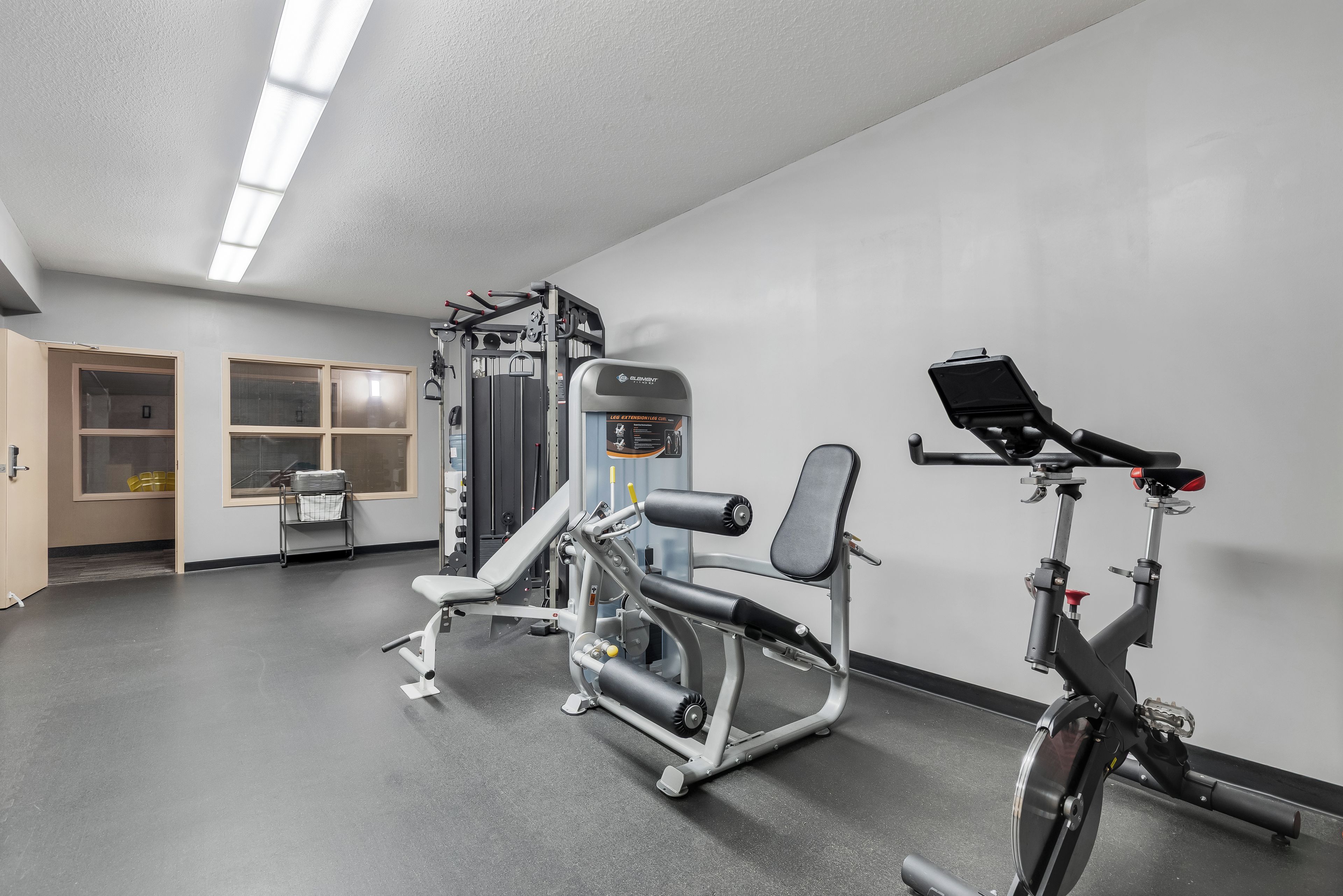 Un gimnasio con equipo de ejercicio, una bicicleta y una puerta que da a un área de almacenamiento.